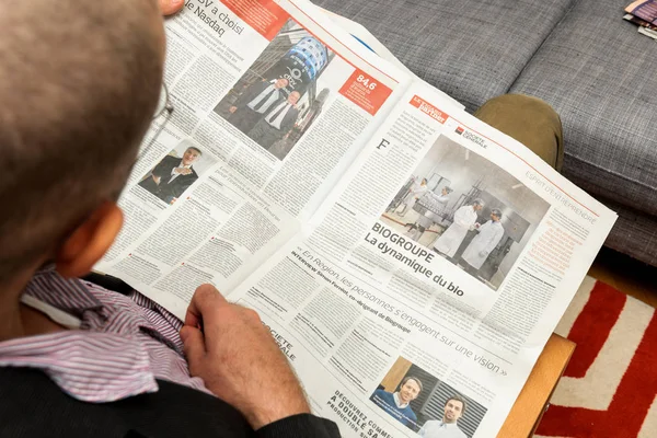 Hombre leyendo sobre las evoluciones de los negocios franceses en el periódico — Foto de Stock