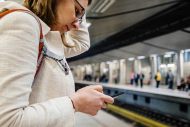 Tren bekliyorsun ve Puan, commuting için arama bir smartphone cep telefonu ile mobil internet sörf kadın gezi ve ziyaret yerleri Atina metro istasyonunda haritalar