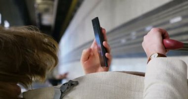 Metro istasyonundaki bir kadının dikey görüntüsü metro istasyonunda cep telefonundan kontrol ediliyor program, sosyal ağ iletileri, mesajlar, web sayfası, haritalar.