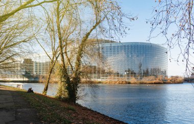 Kadın içinde belgili tanımlık geçmiş - sakin hasta nehir etkileyici cam cephe bina Avrupa Parlamentosu hükümeti ile waterside hasta nehrin yakınlarında bir kitap okuma