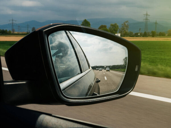 Mountains and cars and highway seen in the rear-view mirror of a