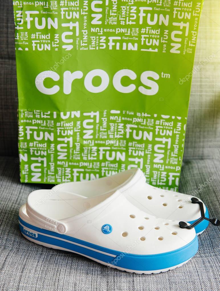 PARIS, FRANCE - OCT 27, 2016: Pair of new Crocs foam clogs and their green paper bag on gray background. Crocs is a worldwide company selling comfortable shoes