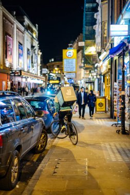 Night food delivery by Deliveroo biker in busy city  clipart