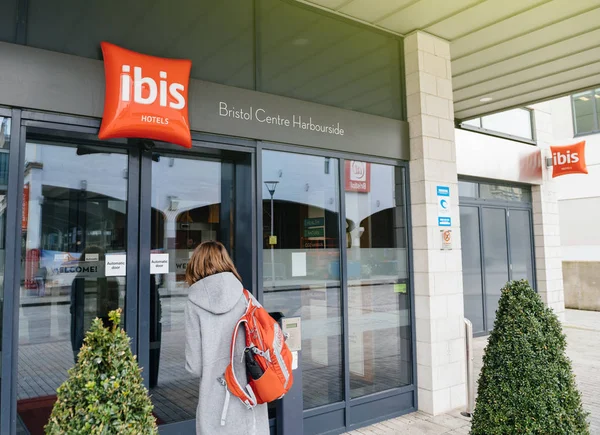 Женщина входит через вход в отель ibis с красной вывеской и дизайнерскими деревьями и красной дорожкой — стоковое фото