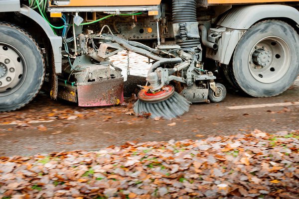 Working orange street sweeper truck on the street working cleaning autumn foliage 