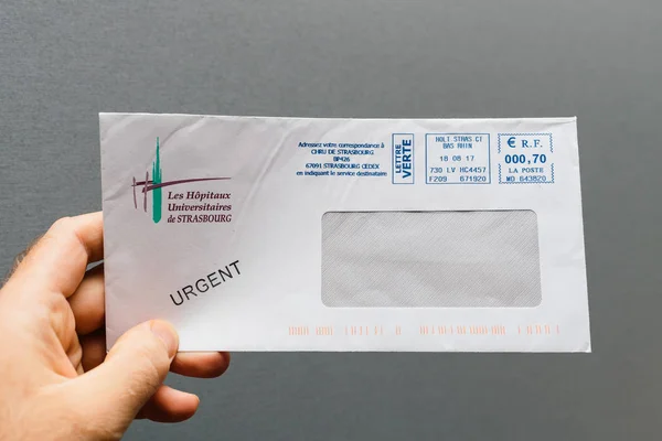 2017年11月28日 人手藏品反对灰色背景一个信封与紧急邮票从斯特拉斯堡大学医院 Hopitaux — 图库照片