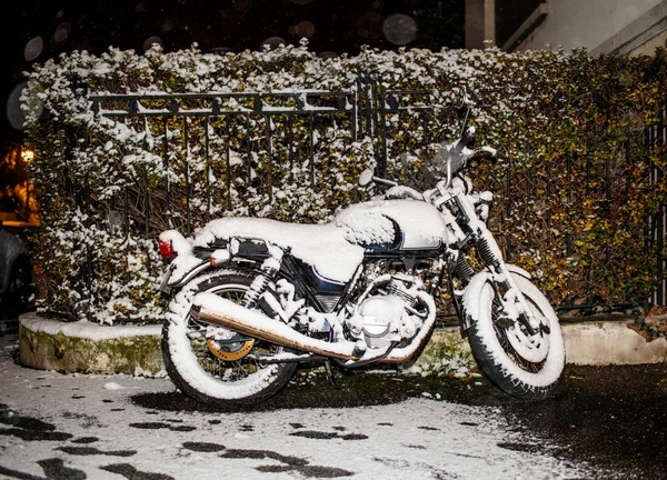 Motorcycle covered with snow at night parked near house