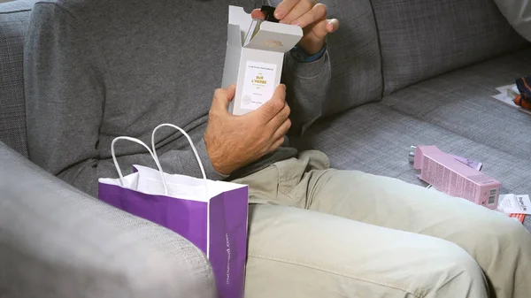 Homem unboxing no sofá cosméticos contendo LArtisan Parfume — Fotografia de Stock