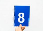 Mužské ruce drží notebook s velkým číslem 8 na modré barvy, 