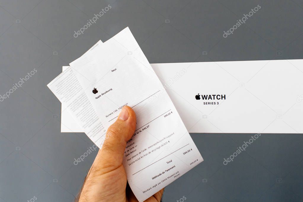 PARIS, FRANCE - APR 15, 2018: Point of view at Apple Watch wearable smartwatch cardboard box in man hand against gray background next to the Apple Store invoice