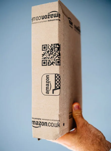Segurando caixa de papelão Amazon contra fundo azul — Fotografia de Stock