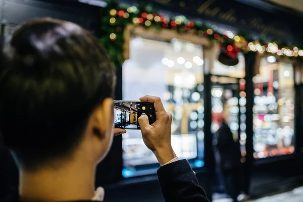 Dospělý muž fotografování na smartphone osvětlené zdobené vitríny — Stock fotografie