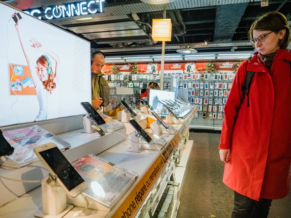 Женщина в красном пальто заглядывает в смартфон магазина Fnac — стоковое фото
