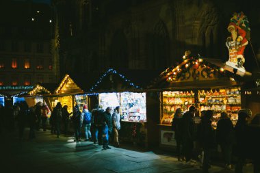 Pazar tezgahlarıyla dolu gece sahnesi. Place de la Cathedrale 'de satılık çok sayıda oyuncakla birlikte. Notre-Dame' da turistler hediyelere ve oyuncaklara hayran kalıyor.