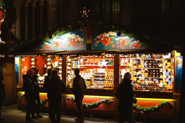 Cena noturna com chalé Market Stall com vários brinquedos à venda na Place de la Cathedrale Notre-Dame com turistas locais admirando o icônico mercado anual — Fotografia de Stock