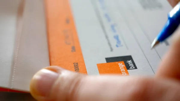 Manos de mujer firmando un cheque bancario en la chequera de Orange Bank — Foto de Stock