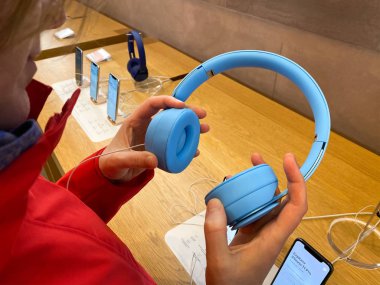 Apple Bilgisayar Mağazası 'ndaki kırmızı ceketli müşteri Dr. Dre Solo Pro Aktif Gürültüyü İptal Eden Kulaklıkları test ediyor.