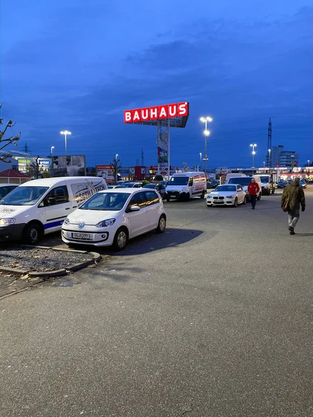 Großer Parkplatz des Baumarktes Bauhaus mit Kunden, die in der Abenddämmerung auf geparkte Autos zugehen — Stockfoto