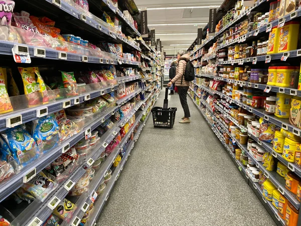 Γυναίκα καλάθι αγορών κοιτάζοντας ράφια προϊόντα τροφίμων στο σούπερ μάρκετ — Φωτογραφία Αρχείου