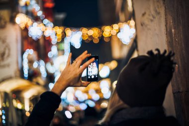 Noel Pazarı için Maroquin sokağının işlek sokağının akıllı telefonunda fotoğraf çeken genç bir kadının arka görüntüsü.