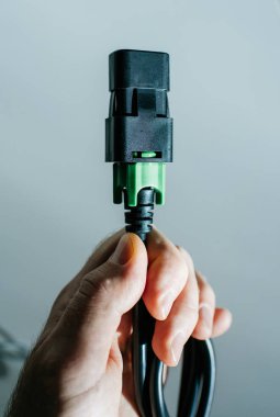 Elinde siyah ve yeşil elektrik kablosu olan bir adam maviye karşı.