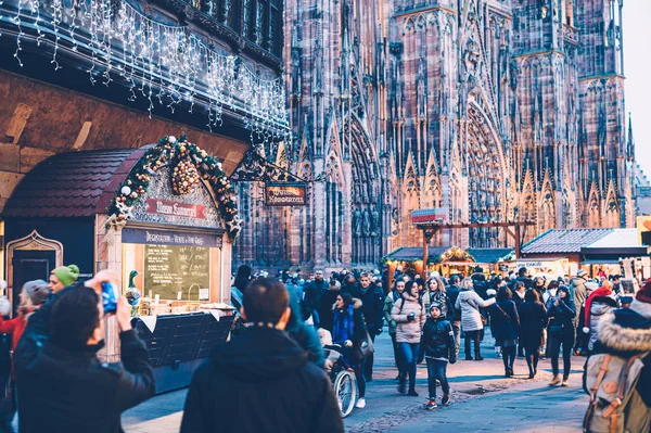 Місцеві жителі та туристи відкривають Різдвяний ринок в центрі Страсбурга з собором Нотр-Дам на задньому плані та хоалетом з їжею від Майсон Каммерцелл. — стокове фото