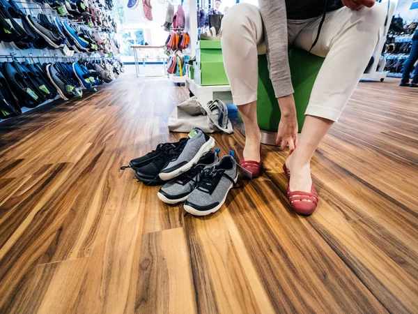 Mujer joven que mide múltiples zapatos Crocs cómodos dentro de la tienda dedicada Crocs - piso de parquet de madera —  Fotos de Stock