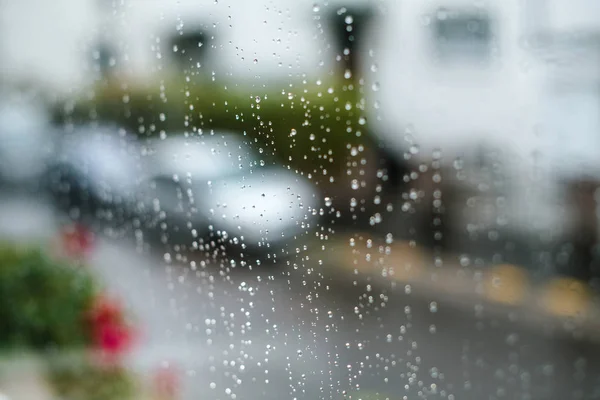 Zbliżenie powierzchni szklanego okna z kroplami deszczu na zewnątrz i rozproszonymi liśćmi sylwetek samochodów — Zdjęcie stockowe