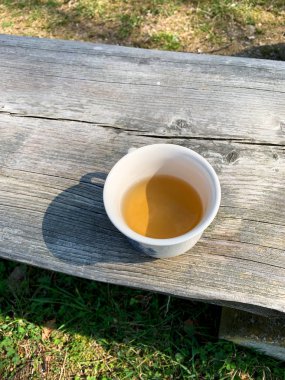 Bahçedeki ahşap bankta sıcak bitki çayı fincanı manzarası