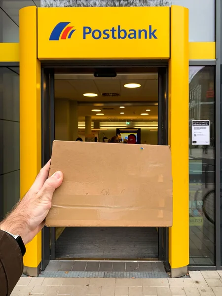 Hombre de mano sosteniendo sobre postal en frente de la oficina postal de Postbank en la ciudad alemana POV perspectiva personal — Foto de Stock