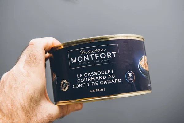 Man hand holding against gray background metallic Canning preserves manufactured by Maison Montfort with French Cassoulet gourmand au confit de canard duck meat with peas — ストック写真