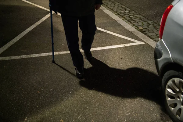 Силуэт и тень пожилого человека, идущего по французской улице ночью с помощью трости, сохраняющей равновесие с голубым телескопическим алюминиевым тростником — стоковое фото