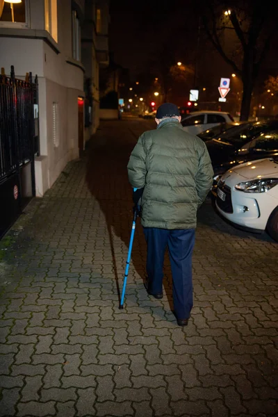 Rer vue de l'homme âgé marchant dans la rue française la nuit en utilisant bâton de marche préservant l'équilibre avec la canne télescopique bleue en aluminium Assistance médicale et de réadaptation — Photo