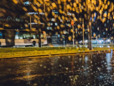 Odaklanamayan yağmurlu bir sokak. Kamu otobüsü hızla giderken arabanın ön camından görülüyor.
