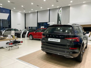Wide angle view of car dealership showroom interior with multiple Skoda Cars inside and focus on black Skoda Kodiaq 4x4 SUV clipart
