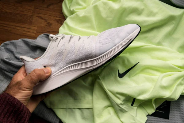 Pov man hand holding at looking at new white professional running shoes manufactured by Nike Zoom Rival Fly for women with multiple pro-clothing in background — 图库照片