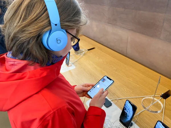 Side view woman in red coat inside Apple Computers Store testing listening to music with new latest Beats by Dr Dre Solo Pro Active Noise Cancelling headphones — 스톡 사진