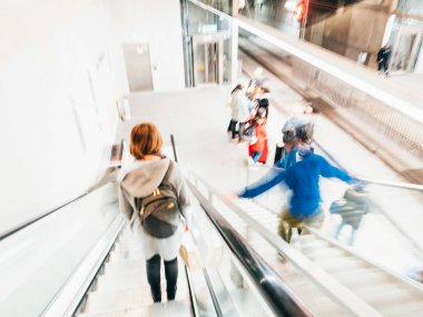Yürüyen merdiven ve metro platformundaki insanların bulanık siluetleri ile odaklanmış görünüm