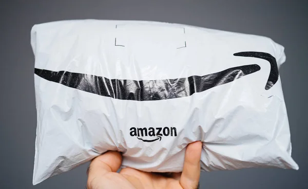 Mano de hombre sosteniendo sobre fondo gris paquete recibido fresco por Amazon Prime con el logotipo de flecha sonrisa —  Fotos de Stock