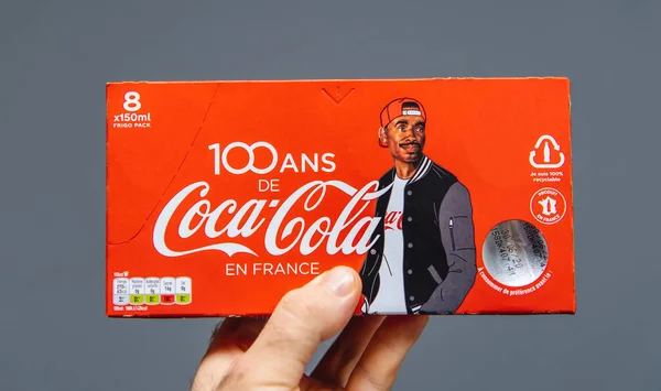 Man hand holding tegen grijze achtergrond pack van Coca-Cola zoete drank 8 pack - Franse editie met 100 jaar aanwezigheid in Frankrijk en zwarte etniciteit man op de cover — Stockfoto