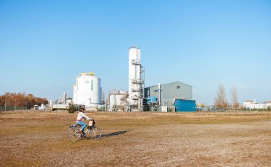 Bisikletli bir kadın, Port de Strasbourg 'daki Prodair gaz fabrikasının yanında açık mavi gökyüzü ve güvenlik çiti koruması altında.