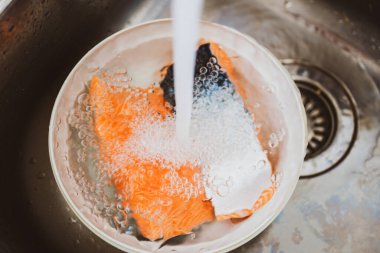 İki parça taze organik somon içeren plastik kasenin üzerine su dökülüyor.