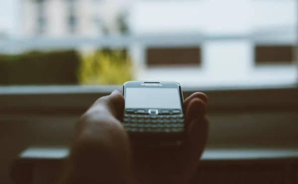 Vintage-Film über Pov männliche Hand hält in Handfläche Vintage Blackberry Profi-Smartphone mit Fokus auf den Schriftzug mit der Tilt-Shift-Linse und großem Fenster im Hintergrund — Stockfoto