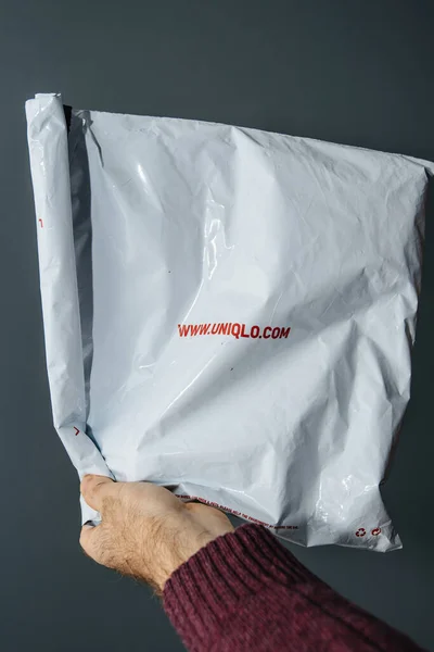 Мужчина держит посылку пластиковый пакет от Uniqlo японской розничной торговли моды - серый фон — стоковое фото