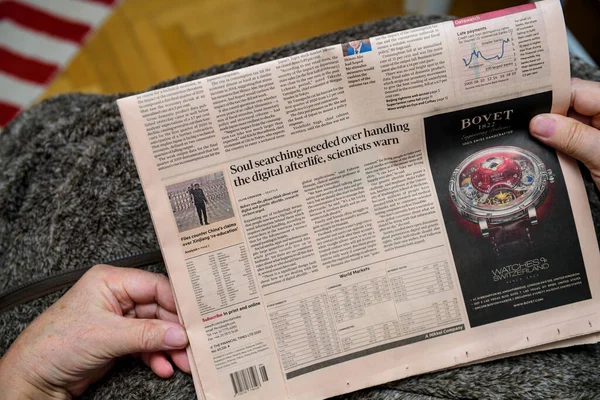 Pov of senior hands holding latest Financial Times newspaper featuring article about soul searching in digital afterlife and Bovet advertising. —  Fotos de Stock
