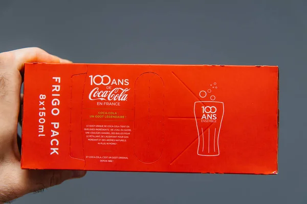 Mano de hombre sosteniendo sobre fondo gris paquete de bebida dulce Coca-Cola 8 pack - Edición francesa con 100 años de presencia en Francia —  Fotos de Stock