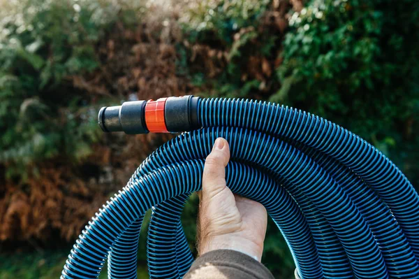 Ouvrier professionnel main mâle tenant montrant sur fond de jardin vert nouveau tuyau d'aspirateur antistatique bleu pour un outil professionnel — Photo