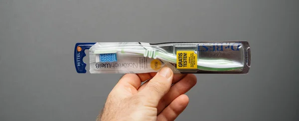 Primer plano mano masculina sosteniendo Dr Mejor cepillo de dientes sobre fondo gris con gran amarillo Gratis testen pegatina alemana —  Fotos de Stock
