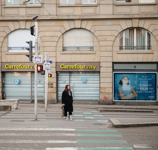 Jong meisje oversteken straat voor Carrefour City supermarkt als Frankrijk worstelt met een uitbraak van coronavirus COVID-19 — Stockfoto