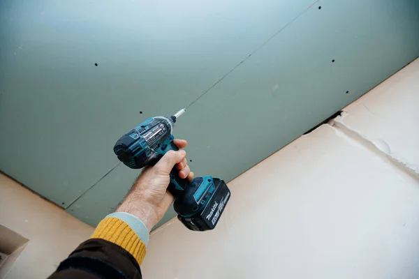 POV male construction hand holding Makita DTD152 18V Cordless Impact Driver with green plasterboard — Stock Photo, Image